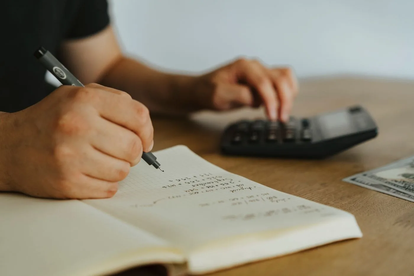 Handen die met een pen en een rekenmachine cijfers in een notitieboek uitwerken